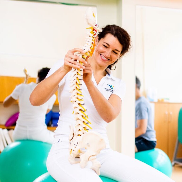 Physiotherapeutin erklärt Behandlungsschwerpunkte anhand eines Wirbelsäulen-Modells